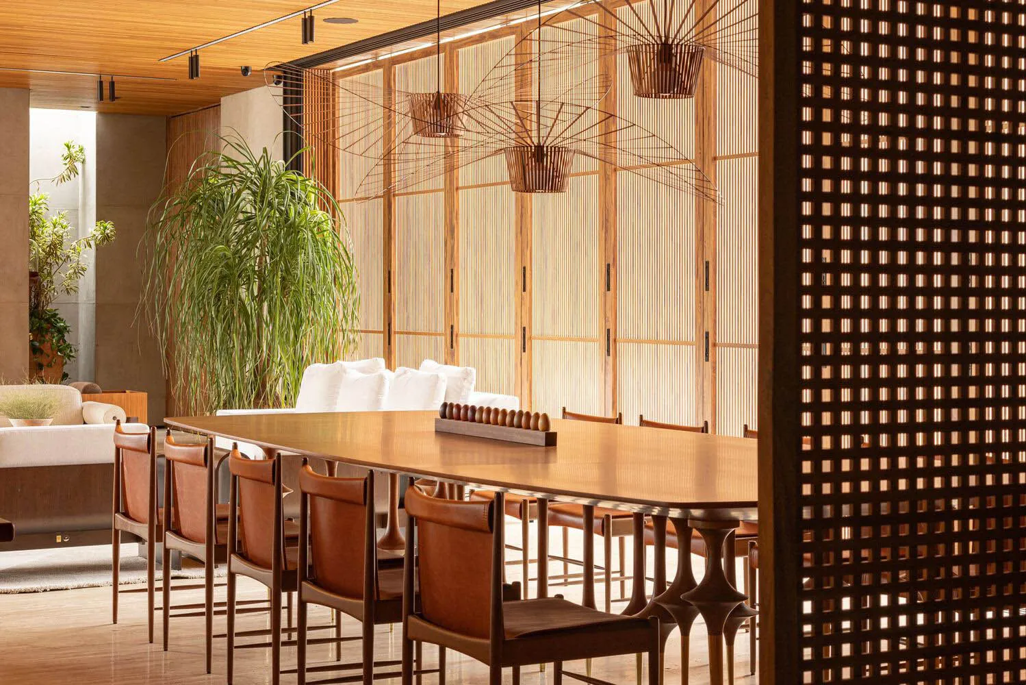 Modern dining space featuring wood and leather furniture, large potted plant, and modern chandeliers.
