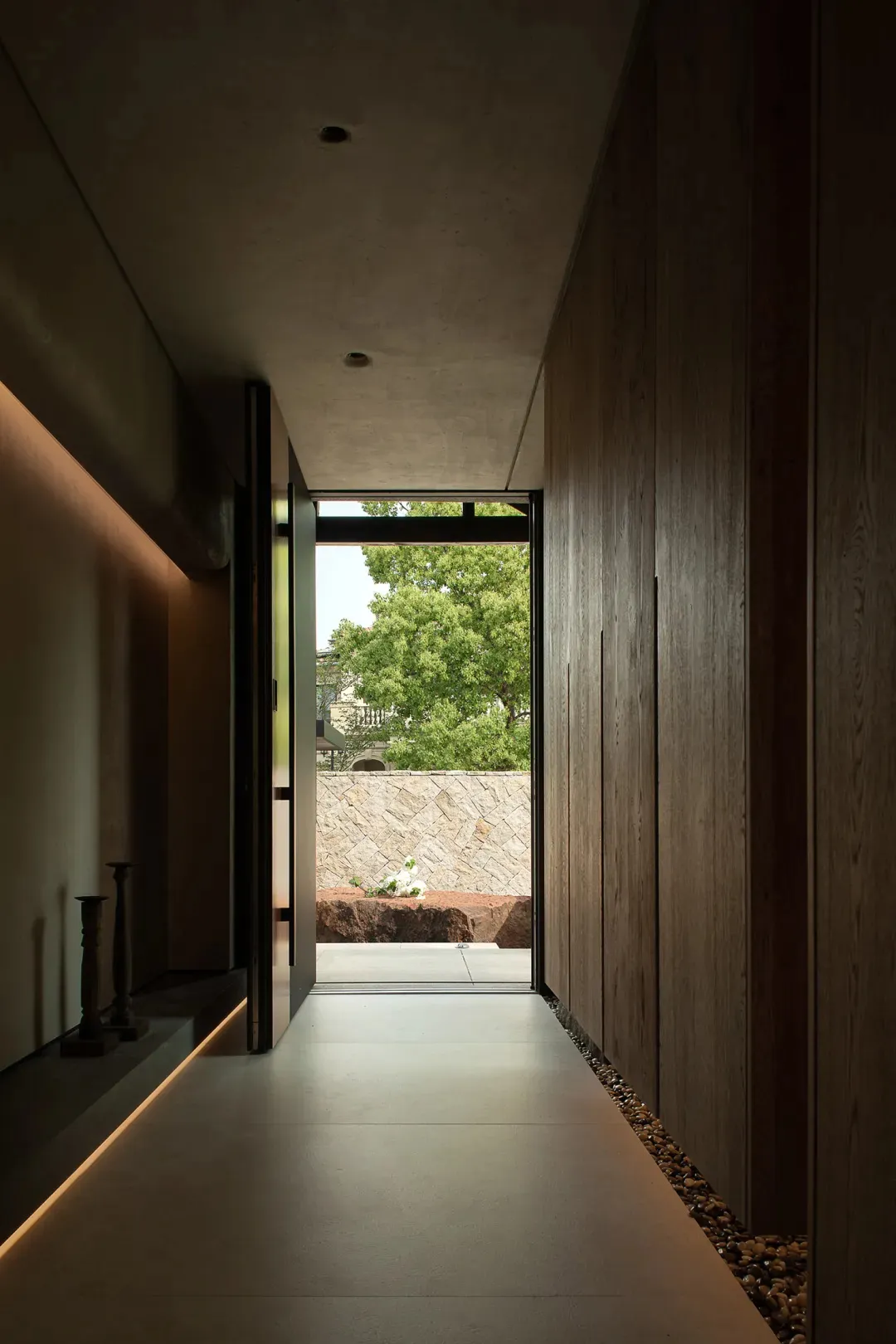 A modern entrance with stone walls and a concrete floor, featuring a window view of greenery.