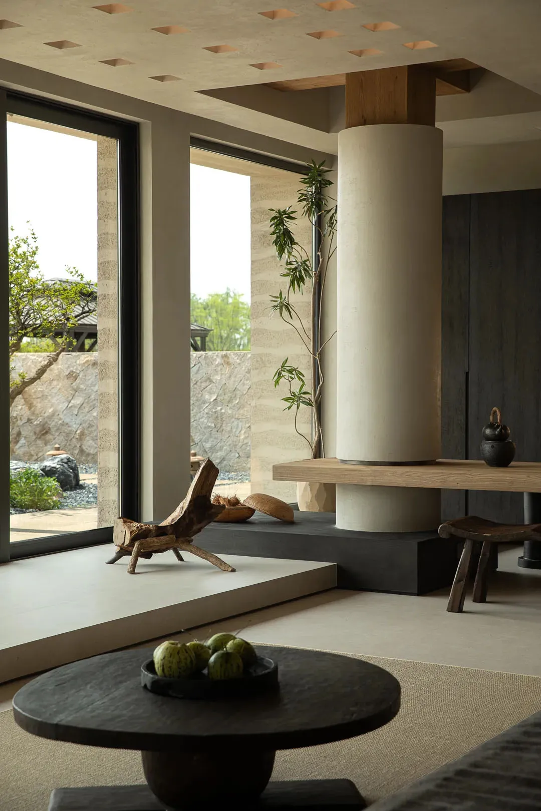 Modern living room with minimalist design, featuring wooden and concrete elements, and a round wooden table with green fruit