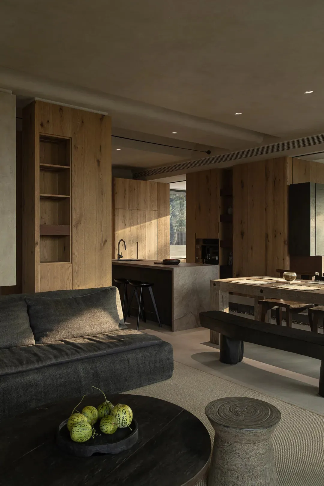 A modern living room featuring wooden furniture, including a grey sofa, a round wooden coffee table, and a wooden dining tabl