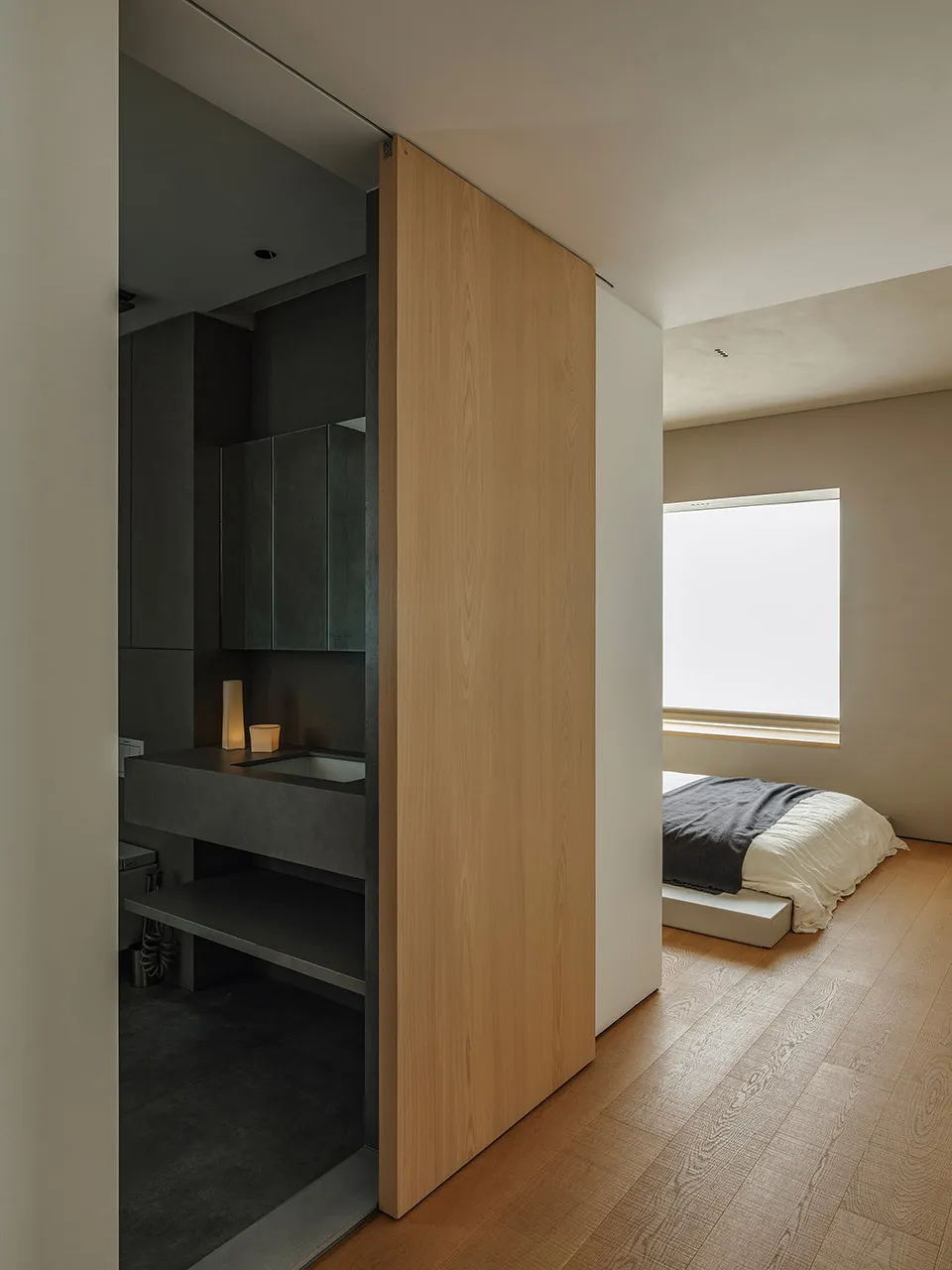 A minimalist bedroom featuring timber and concrete materials with a large window.