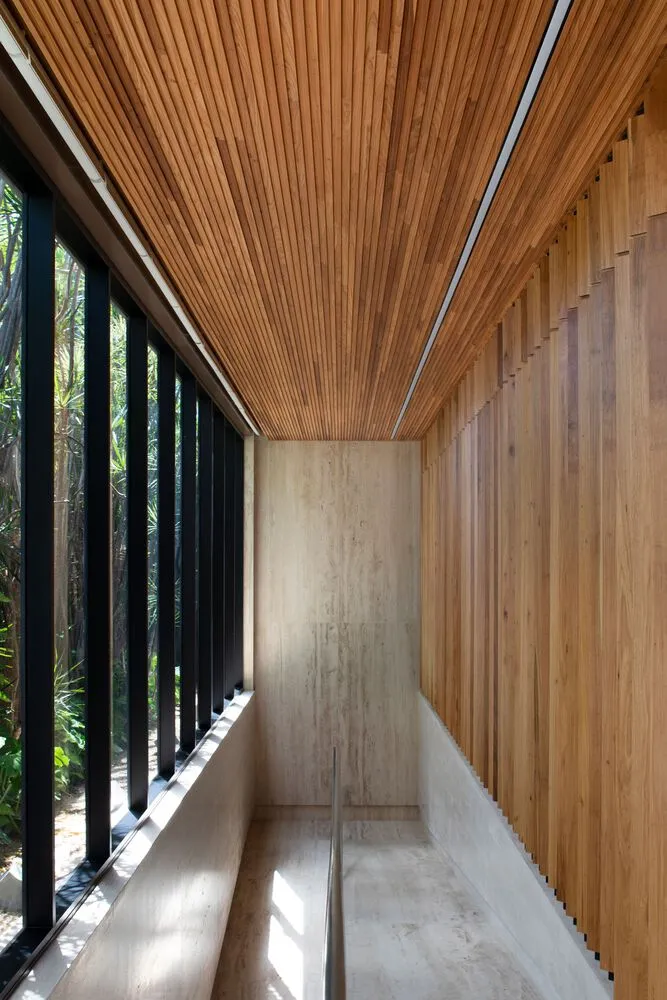 An interior design image showcasing a hallway with wooden walls and ceiling, large windows, and concrete flooring.