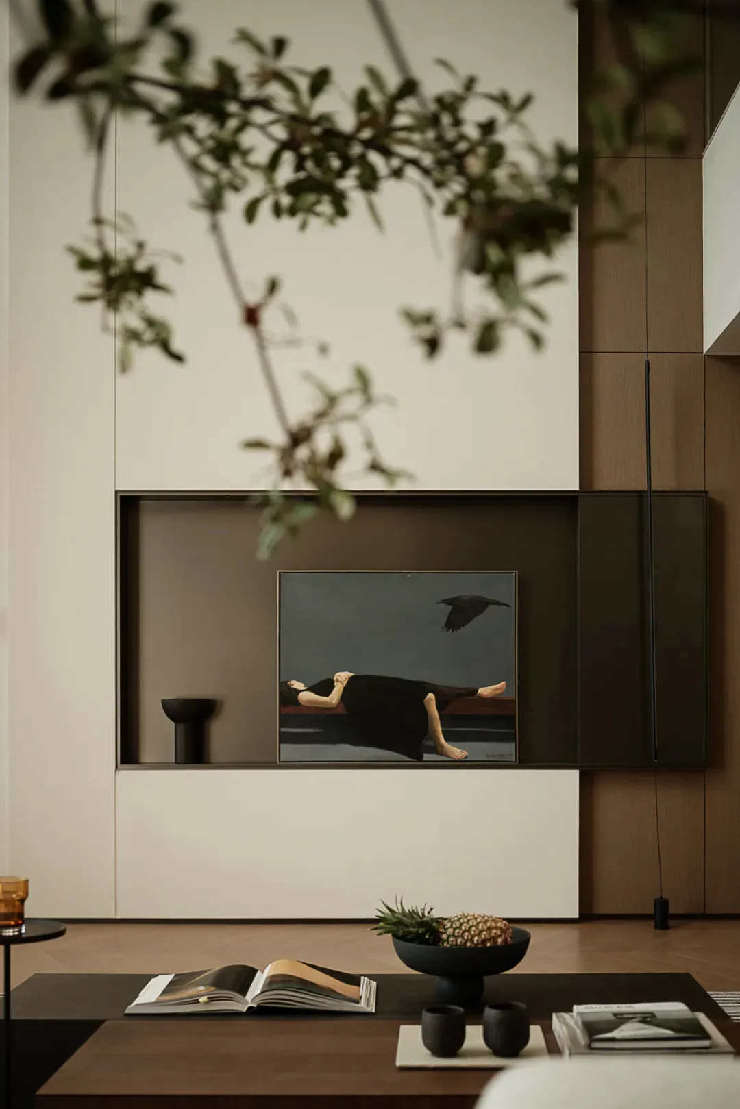 A modern minimalist living room with simple decor, a wooden floor, a black coffee table, and a large wall-mounted artwork fea
