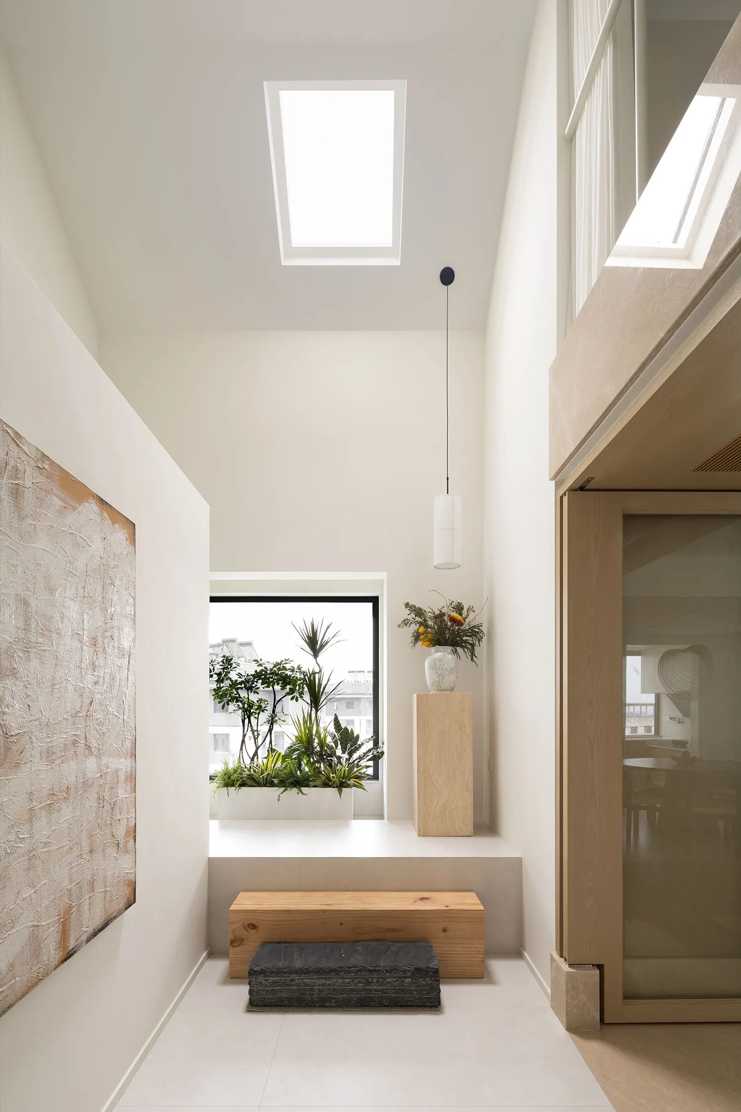 A minimalist interior space featuring white walls, a wooden bench, and glass windows.