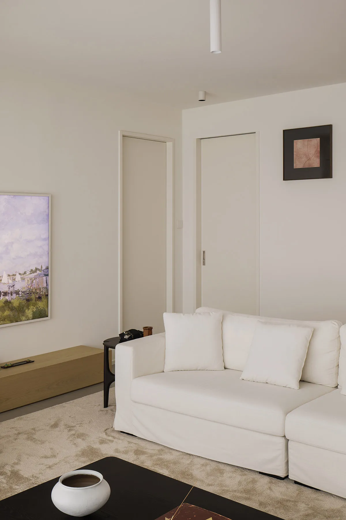 A minimalist living room with a white canvas couch, wooden flooring, and white walls.