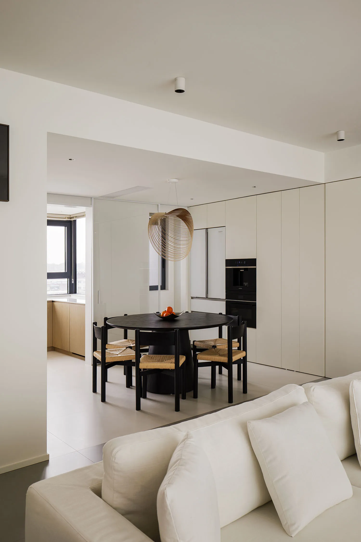A modern kitchen with wooden furniture, a white countertop, and a black dining table.