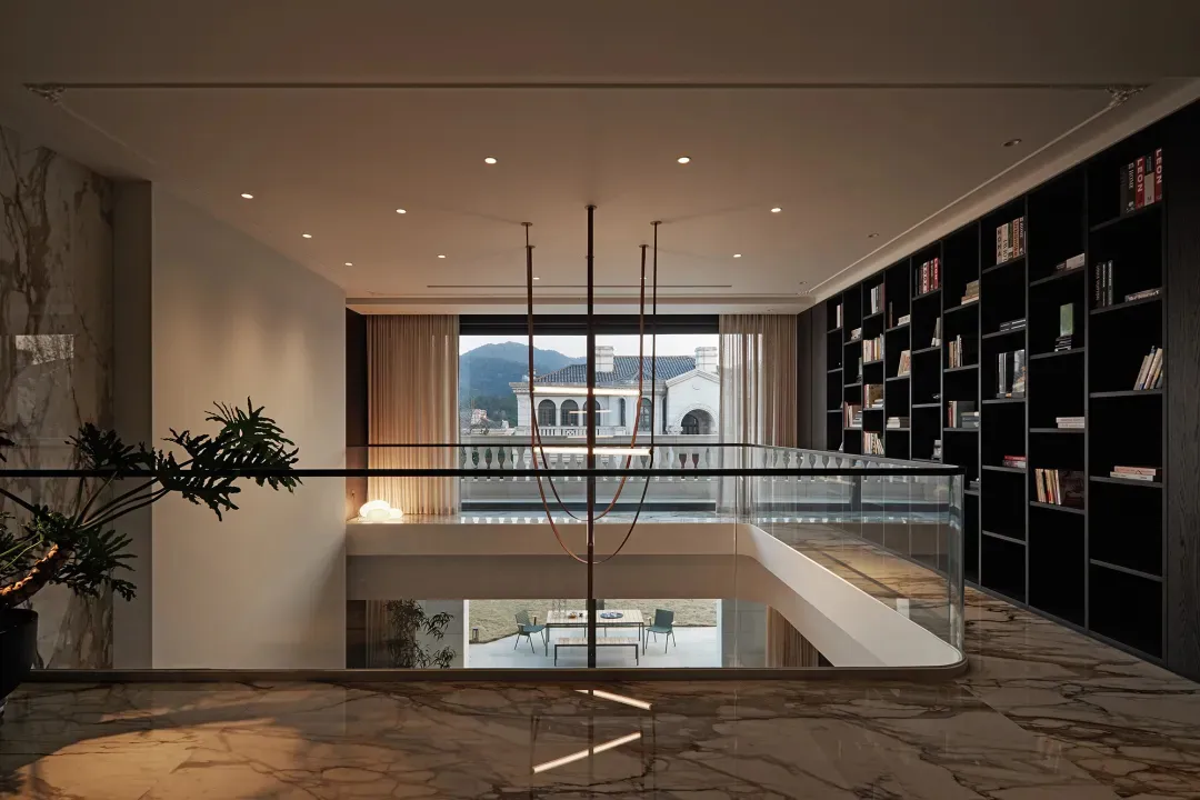 Modern library and balcony with marble flooring, black wooden shelves, and a glass balcony railing.