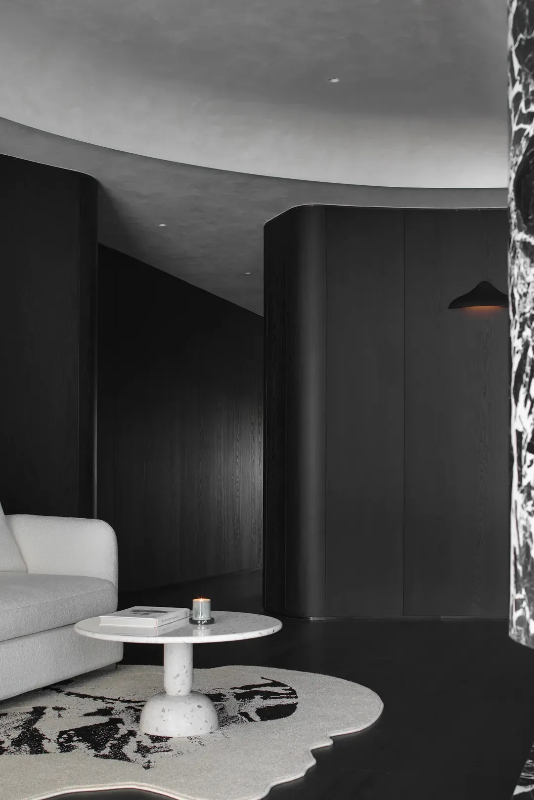 A modern minimalist living room with a white couch and a round marble table on a patterned rug, featuring concrete elements a