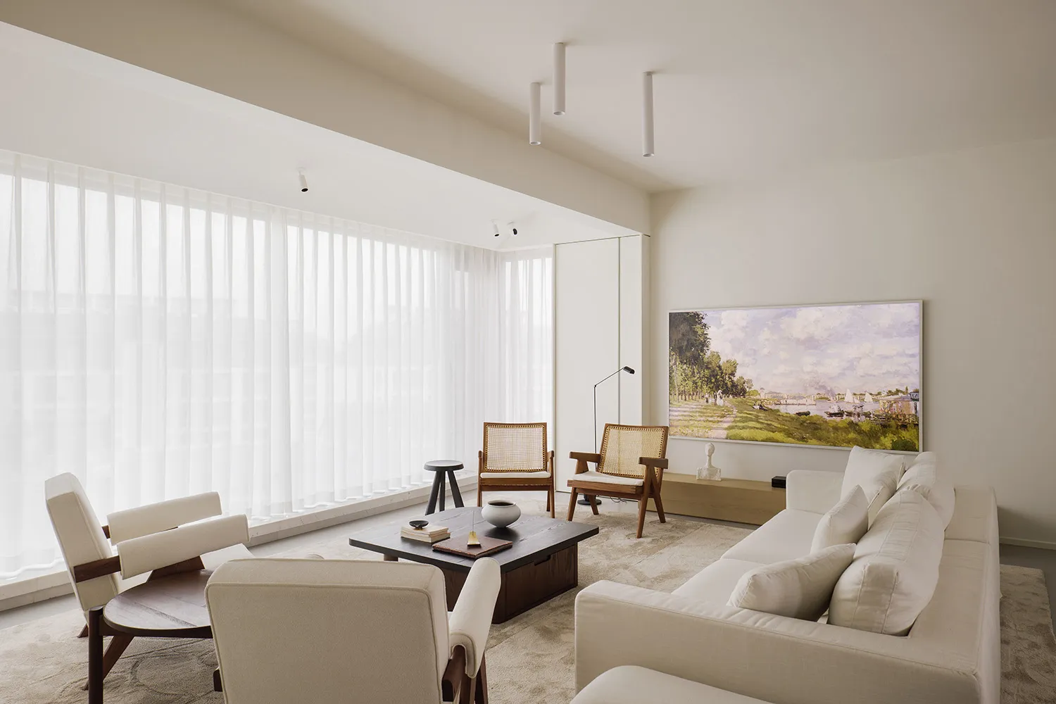 A modern minimalist living room featuring a couch, chairs, and a coffee table with a painting and windows with sheer curtains
