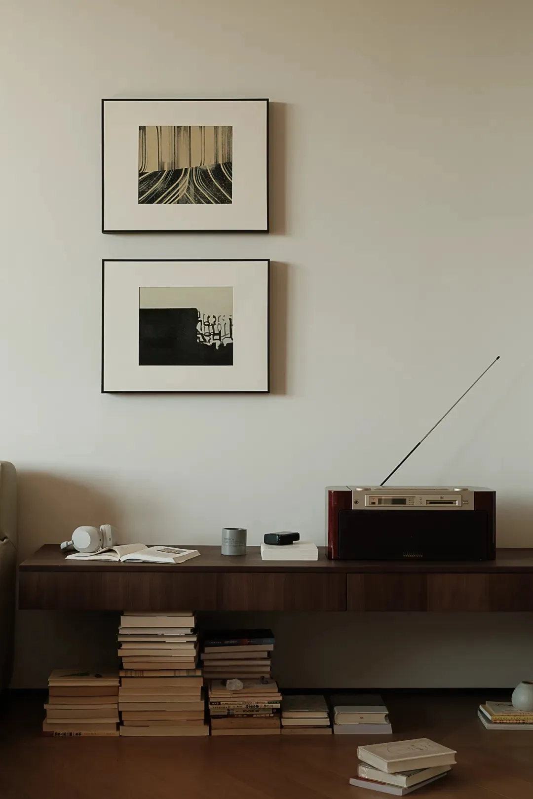 A minimalist living room storage unit with a radio, framed art, and stacked books.