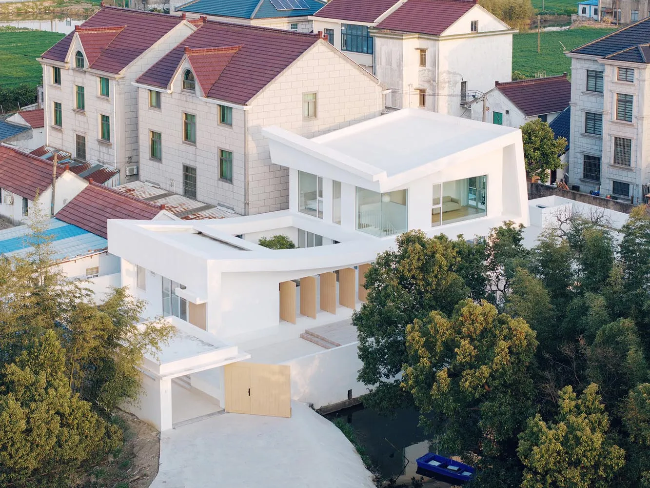 現代住宅建築，外牆採用白色灰泥，環繞綠意植栽。