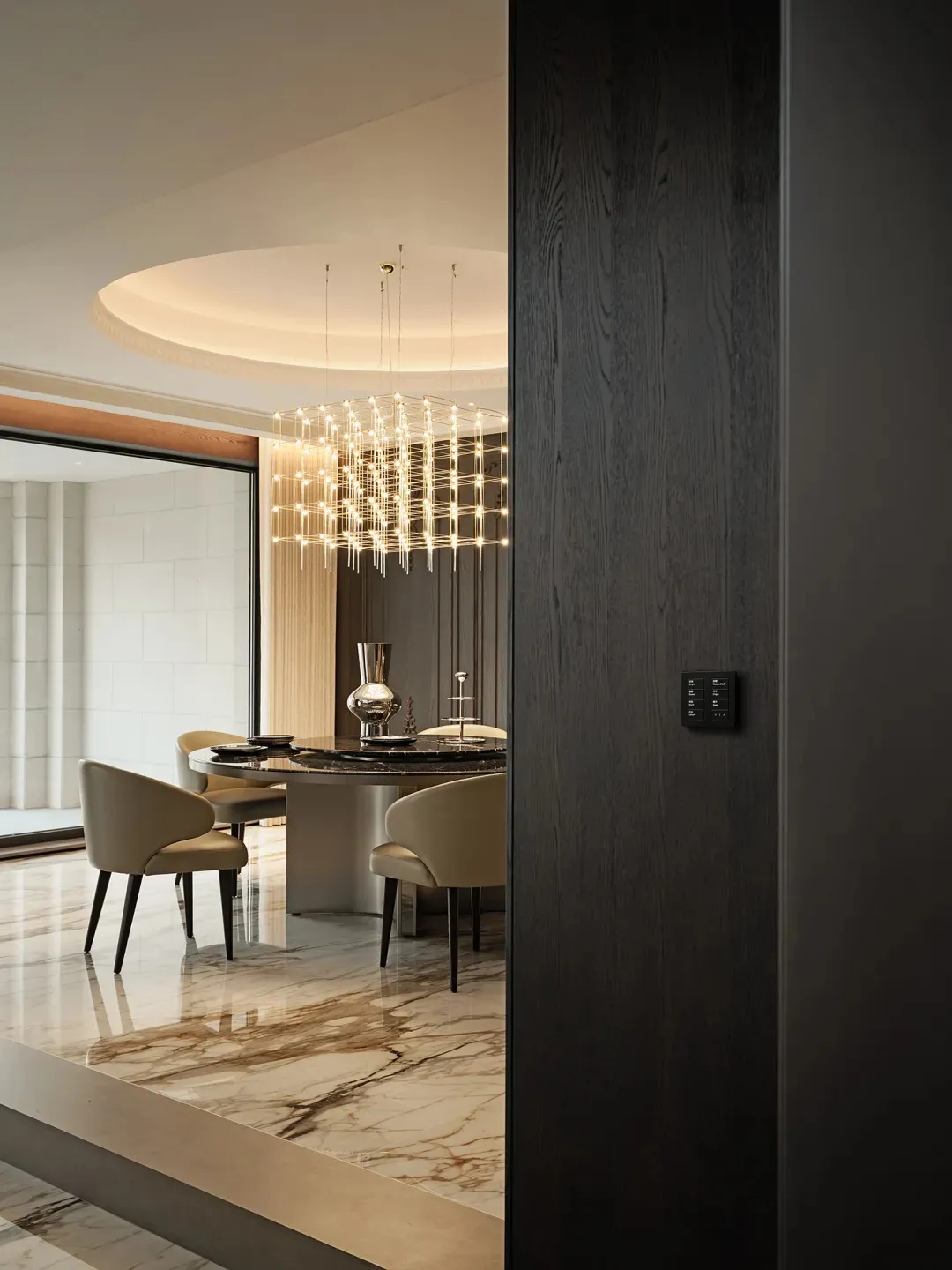 Modern dining room featuring a round table and chairs with marble flooring and a unique chandelier.