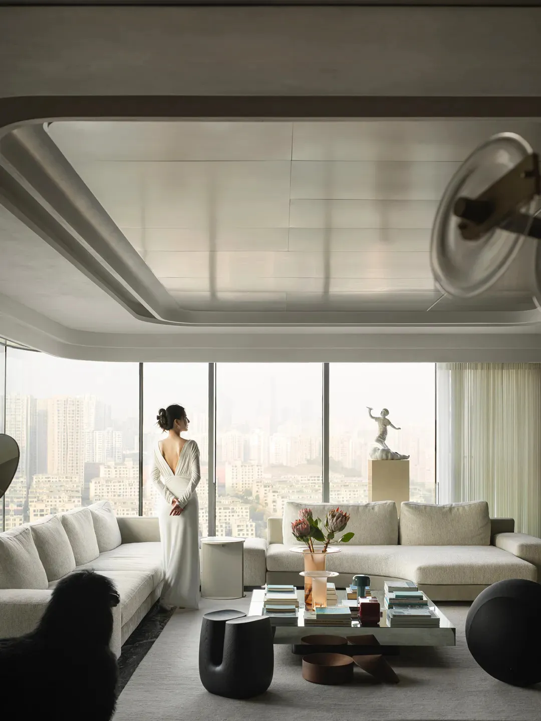 A modern minimalist living room with white fabric furniture, glass tables, metal accents, and marble flooring.
