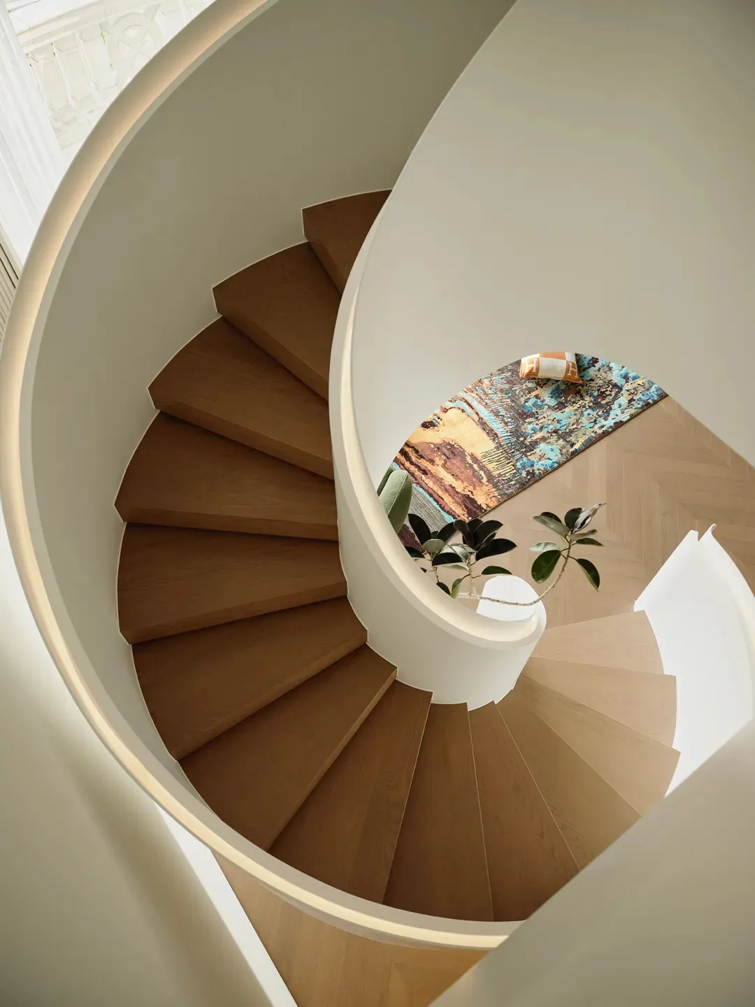 Staircase with wooden steps and a colorful rug at the bottom, viewed from above.