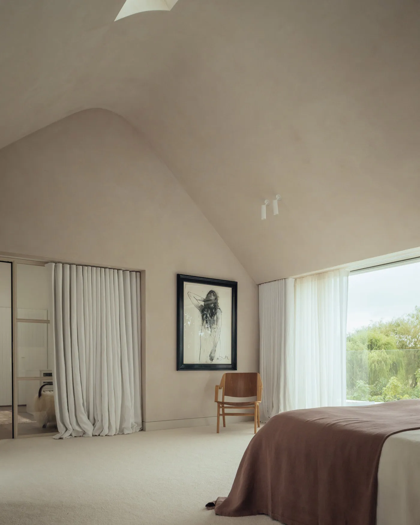 A minimalist bedroom featuring soft textiles, large windows, and a natural light-filled space.