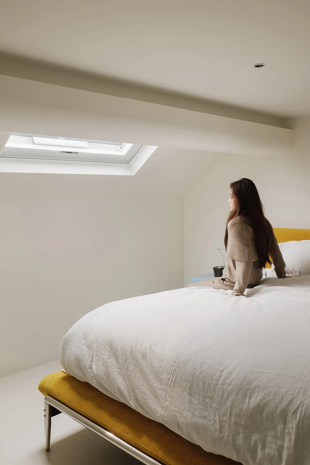 A minimalist bedroom with a white blanket and yellow bed