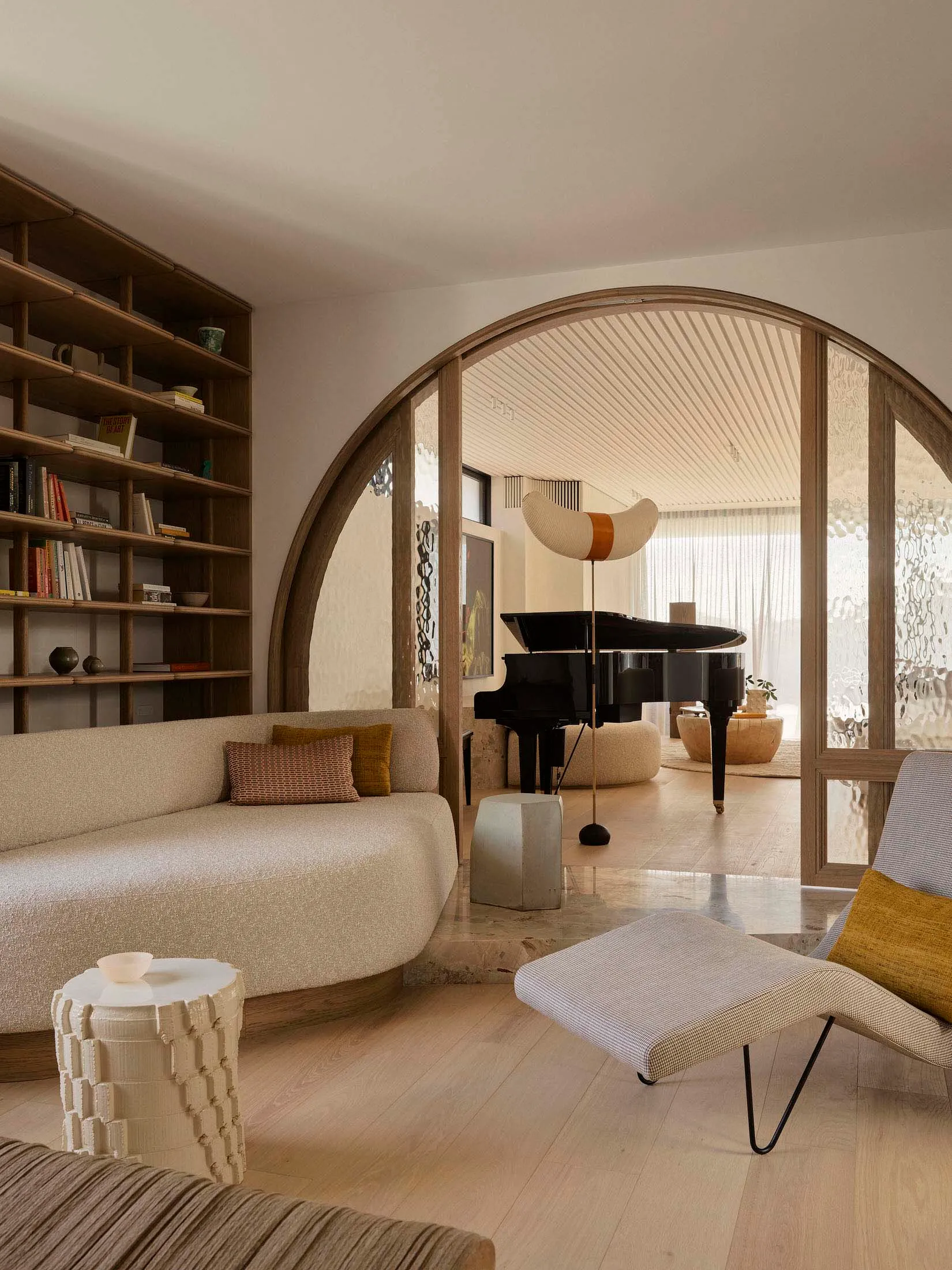 A minimalist living room featuring beige and brown furniture, a grand piano, and a curved wall.