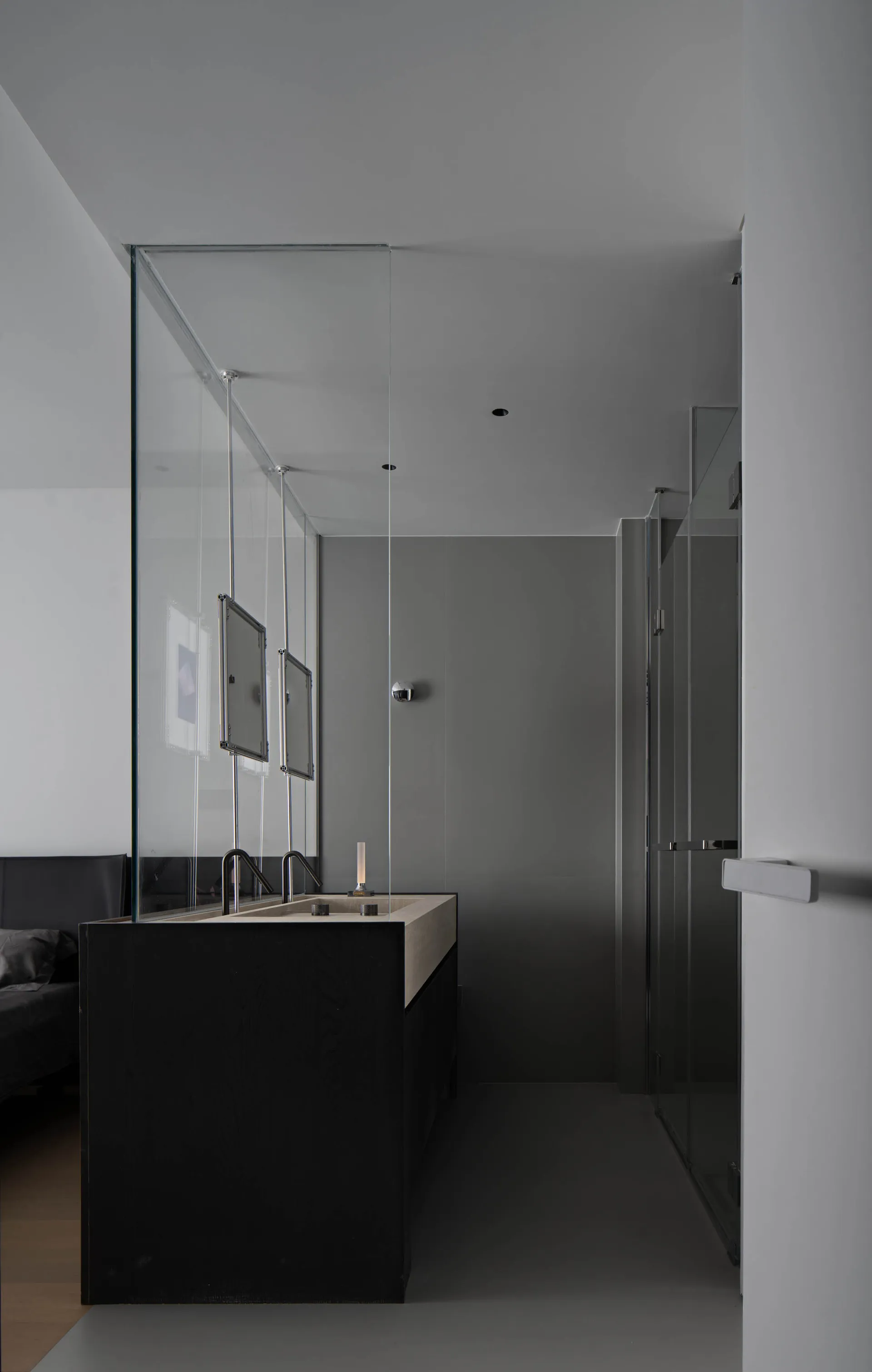 A minimalist modern bathroom with concrete walls and floor, featuring sleek black cabinetry and a long sink counter.