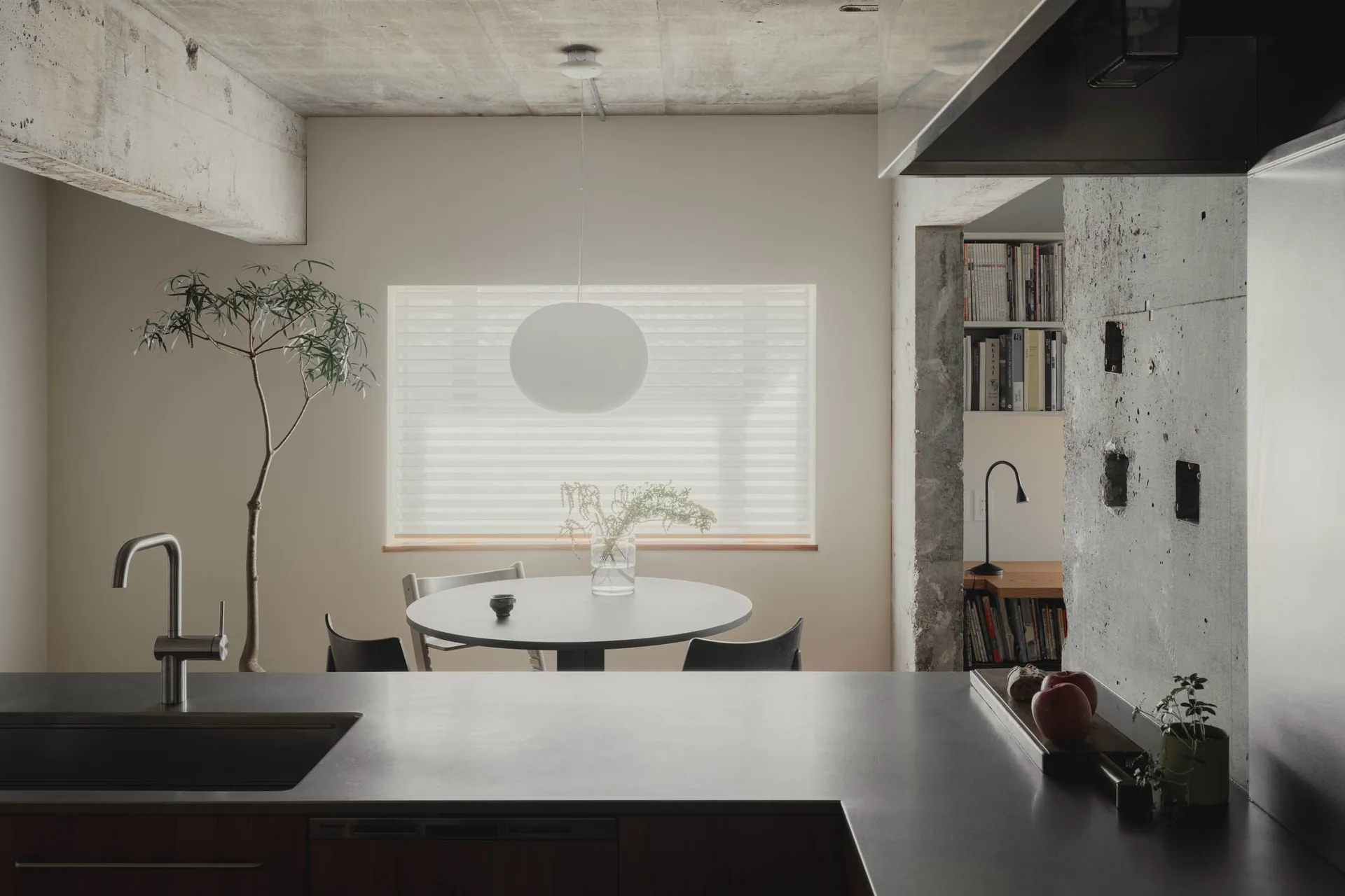 A modern kitchen with a circular pendant light and concrete walls.