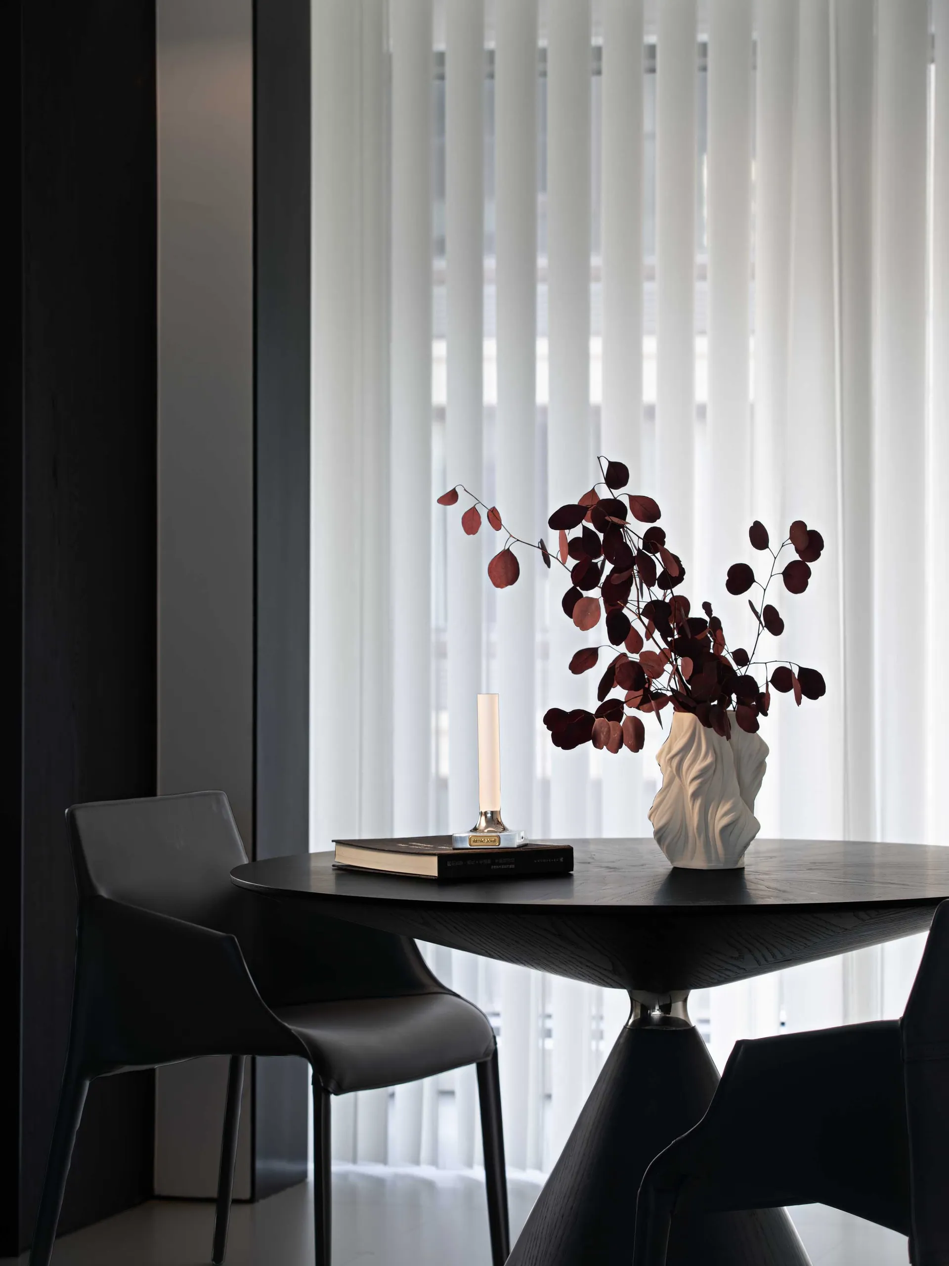 A modern office space featuring black furniture, a vase with red leaves, and a candle.