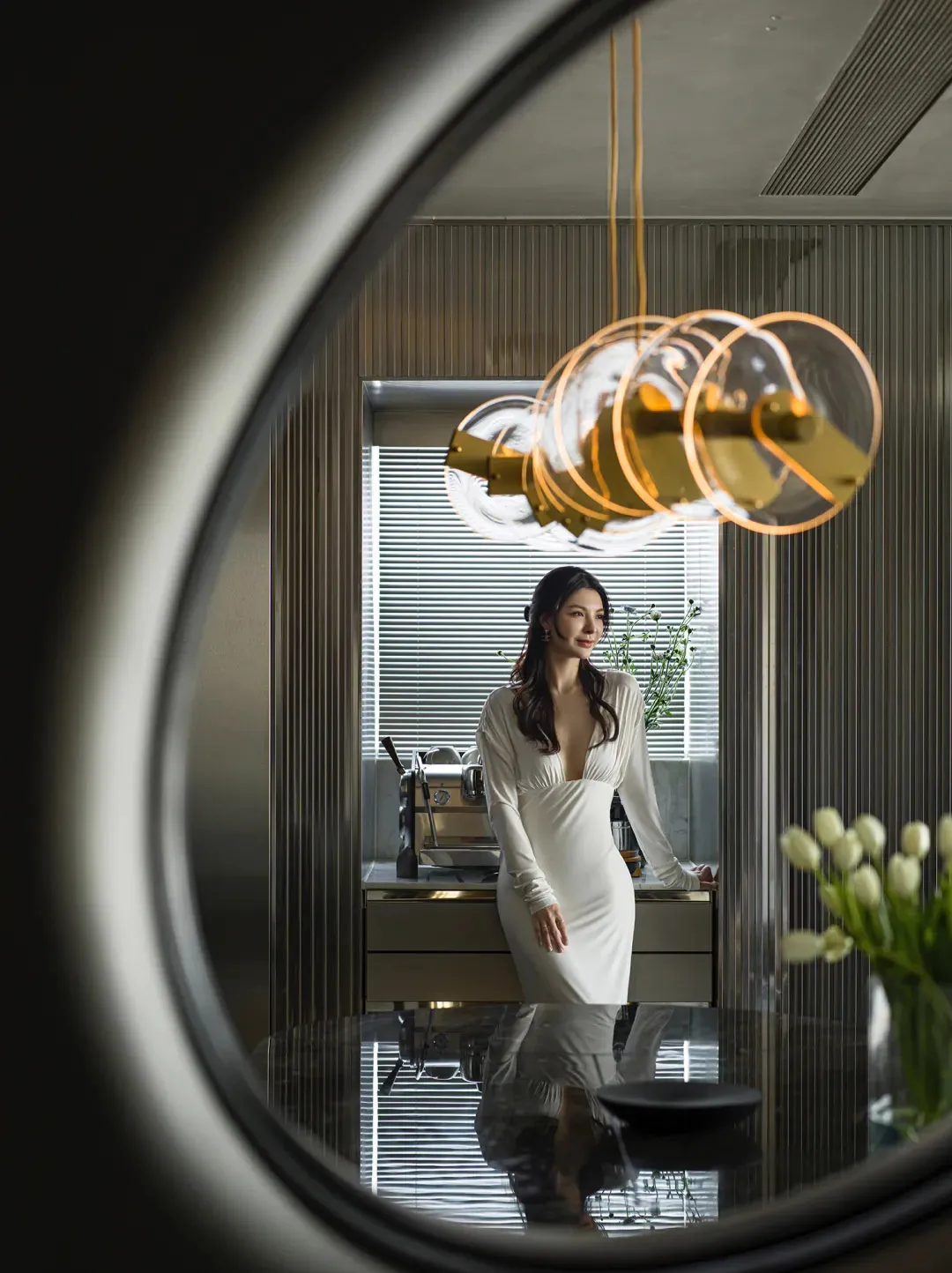 A woman in a white dress standing in a modern residential space with metallic details.
