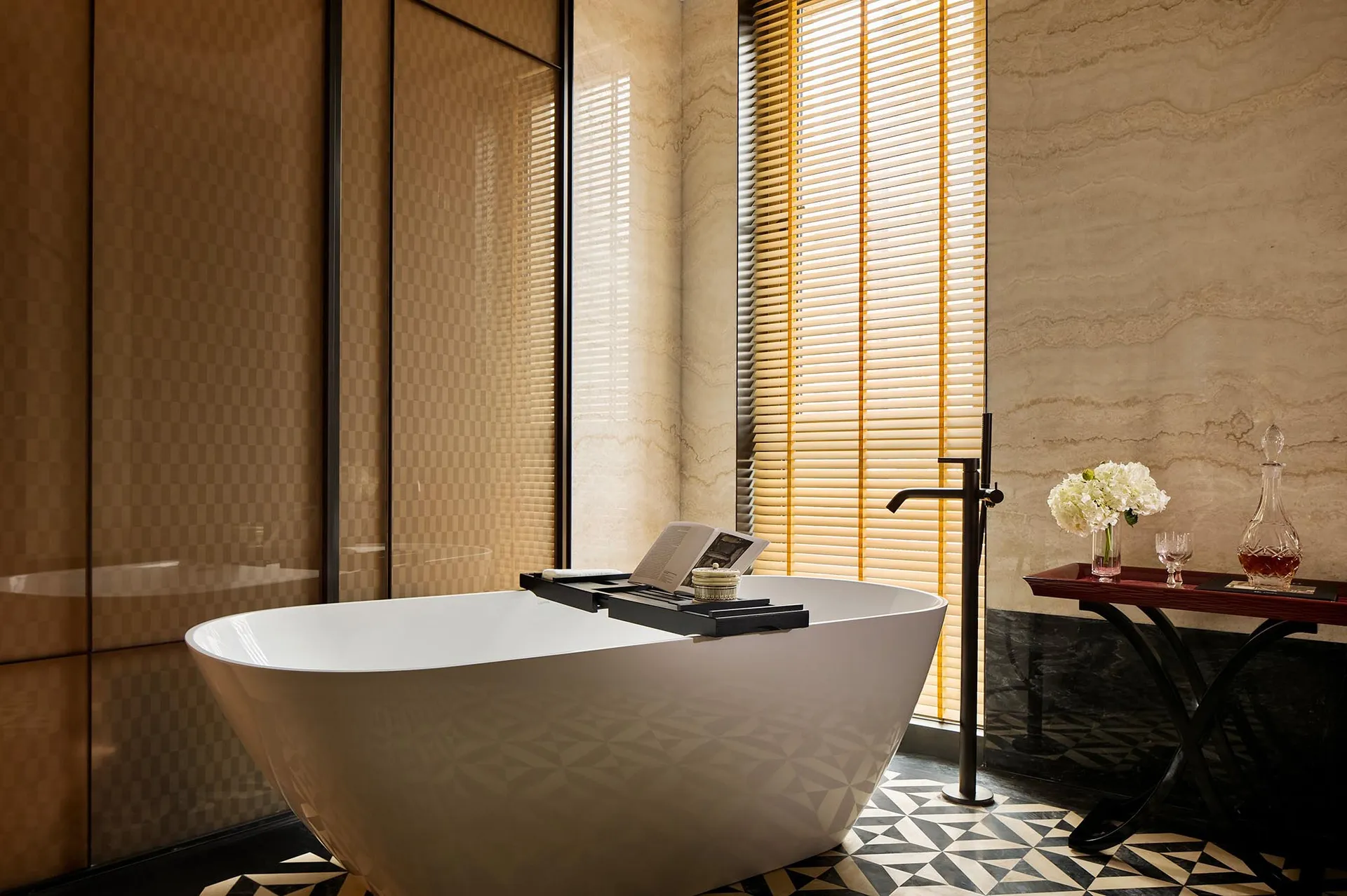 A minimalist bathroom with a freestanding bathtub, marble walls, and a window with blinds.