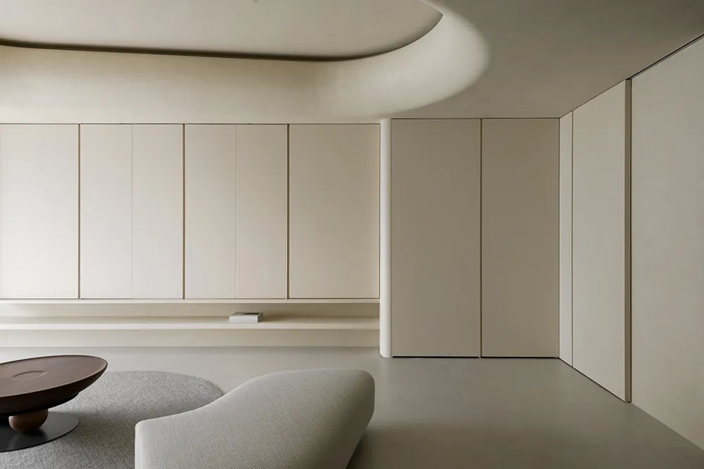 Modern minimalist living room with concrete walls and floor, featuring a curved ceiling and a single wooden table.