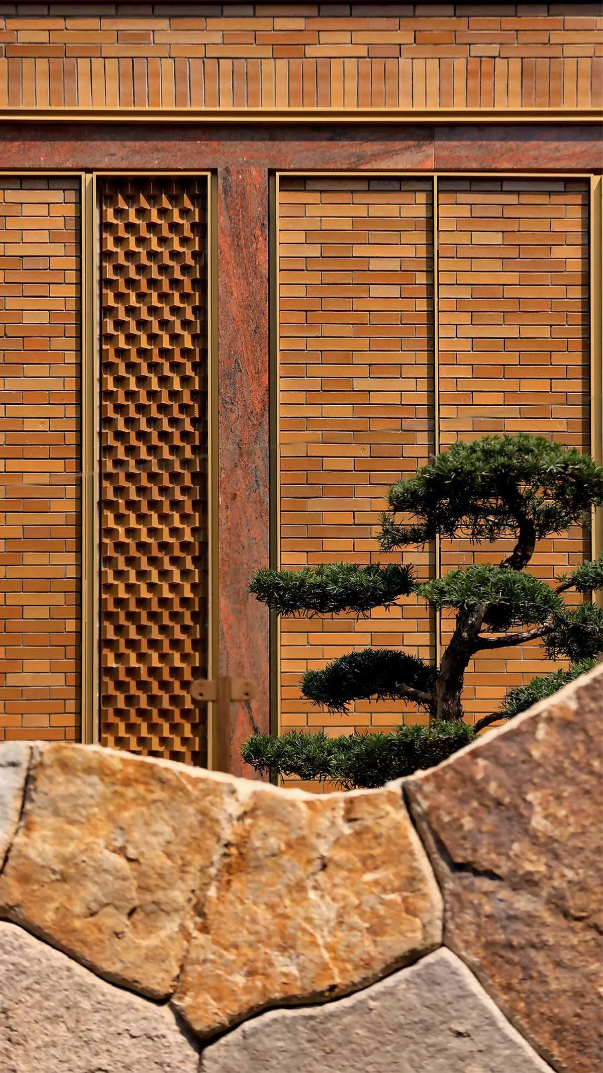 A modern brick wall with a geometric pattern and a small bonsai tree in front of it.