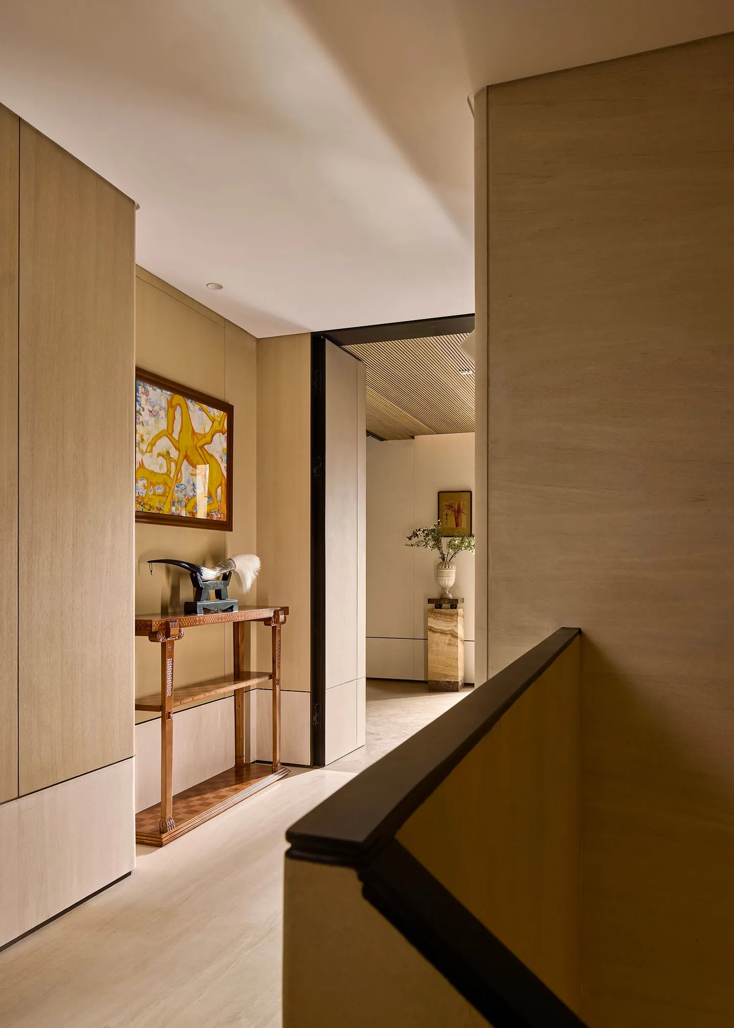 A modern corridor with wooden paneling, leading to a hallway adorned with artwork and decorative plants.