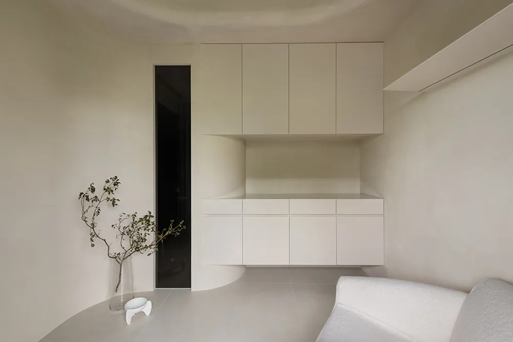 A minimalist kitchen with concrete finishes, featuring sleek white cabinets and a white, textured sofa.