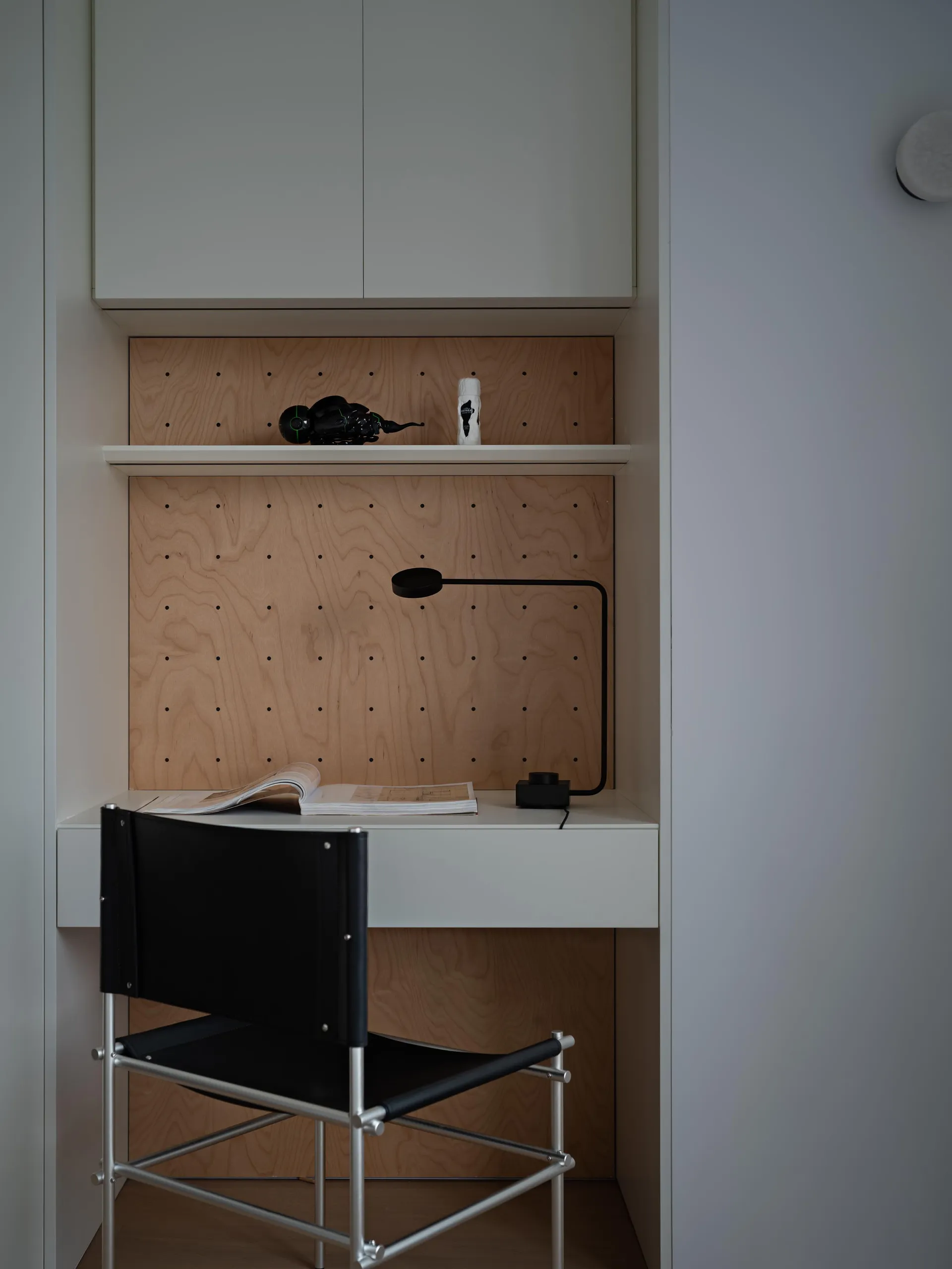 A minimalist study desk with a wooden background, metal frame, and black chair.