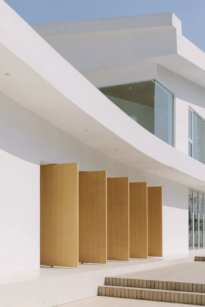 Modern minimalist white building with wooden doors and large windows.