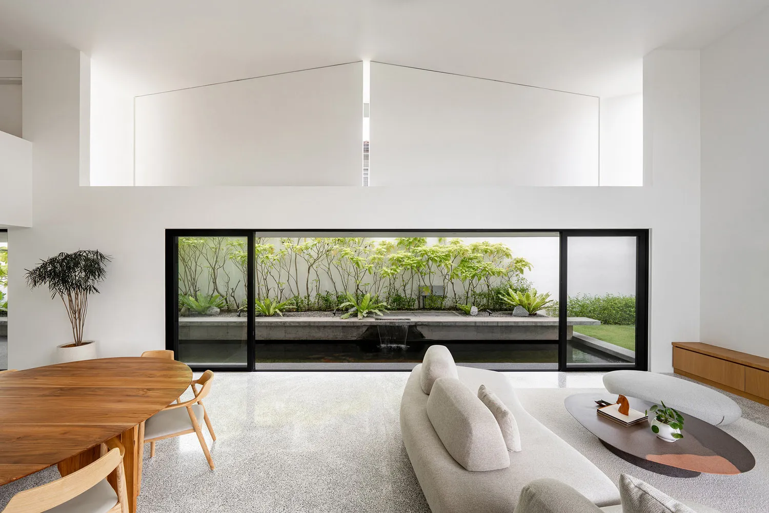 Modern minimalist living room with concrete flooring and large glass windows showcasing a garden view.