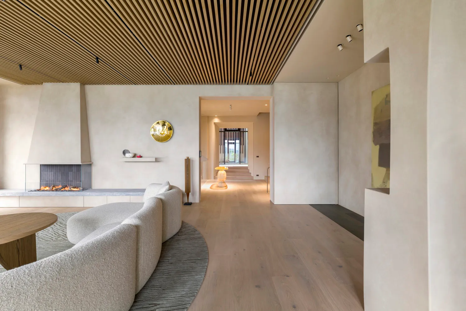 A modern, minimalist living room with white walls, a wood-paneled ceiling, and a fireplace. The space features a comfortable