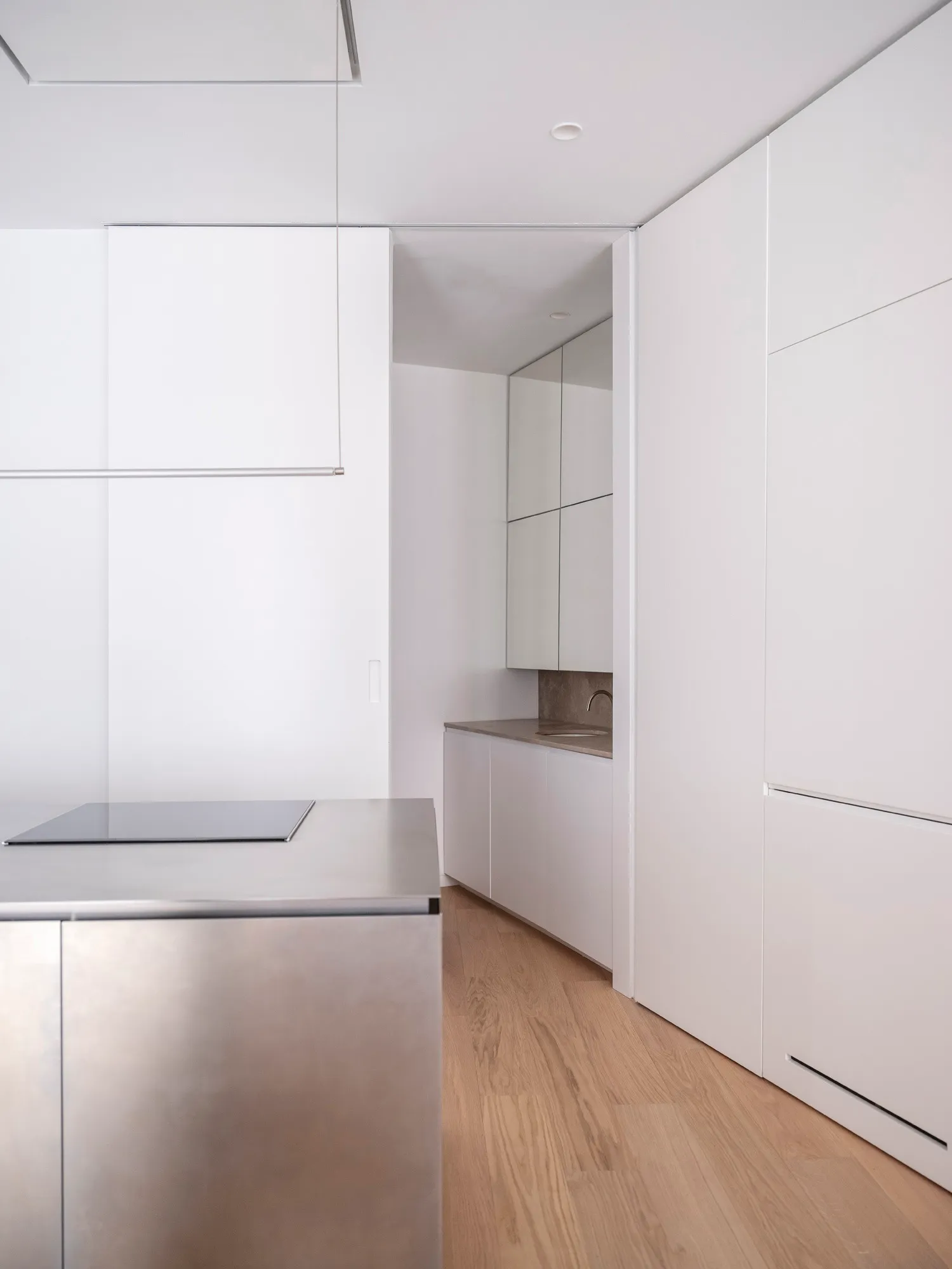Modern minimalist kitchen with white surfaces and stainless steel appliances.