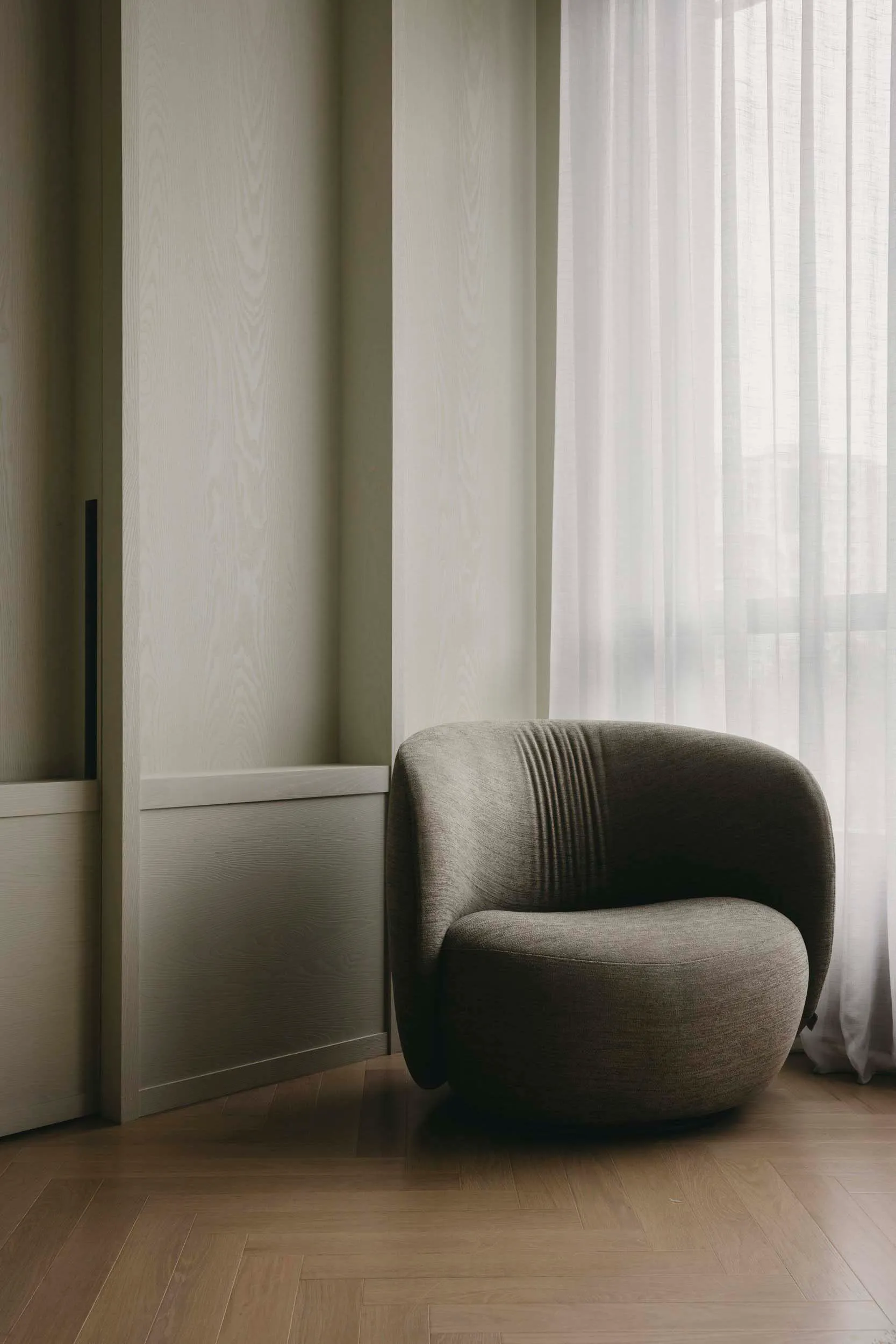 A modern living room featuring a textured fabric chair next to a window with sheer curtains.