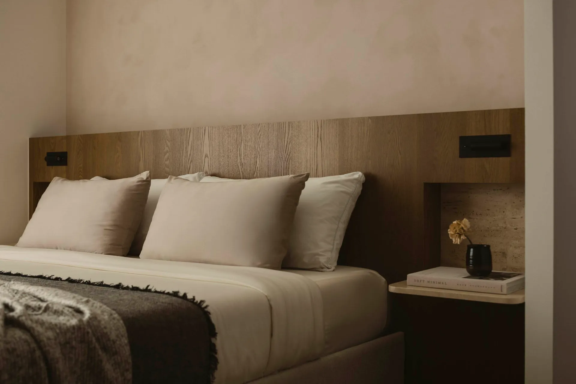 A modern minimalistic bedroom with a wooden headboard and cream-colored bedding.