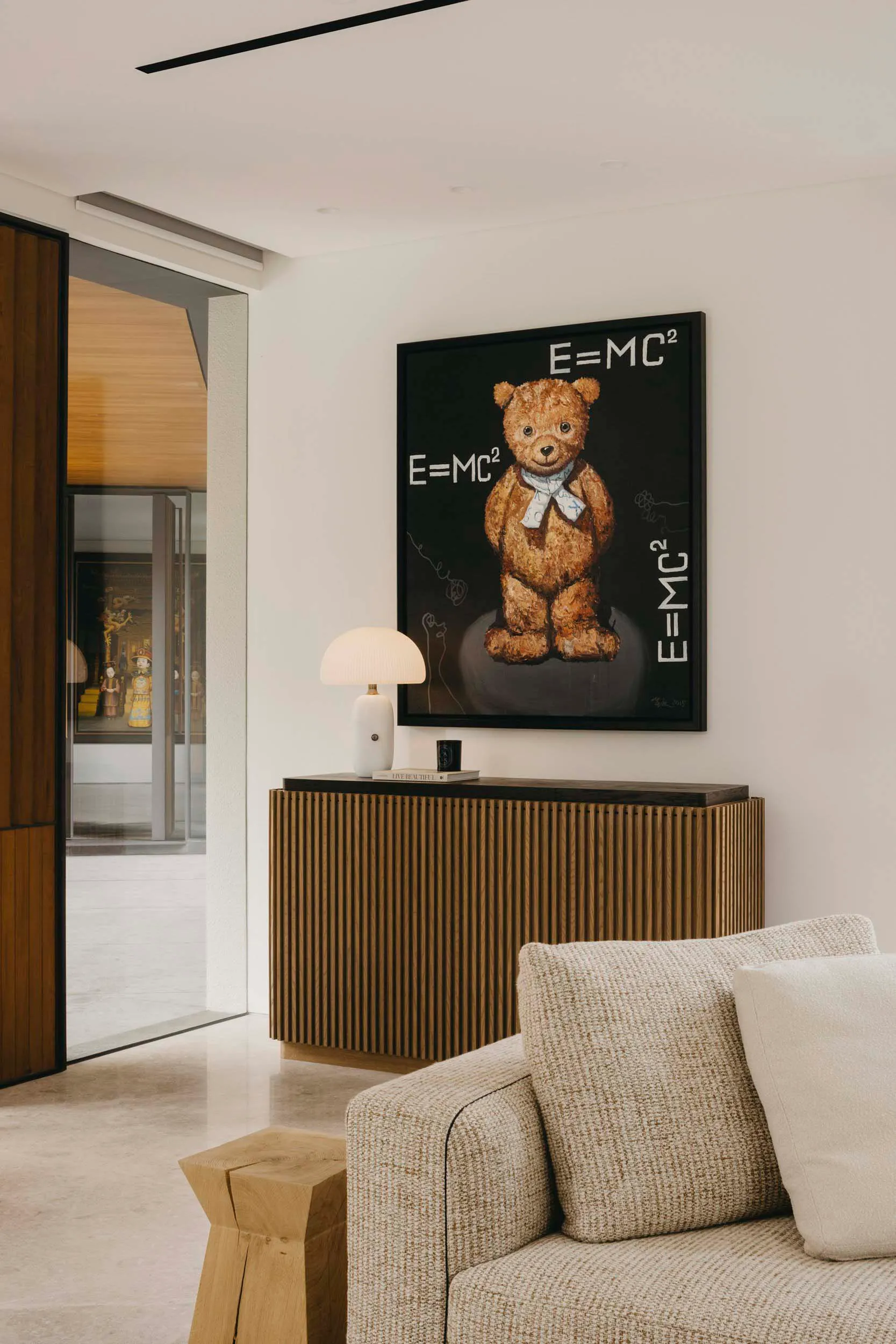Modern minimalistic living room featuring a wooden sideboard adorned with a framed painting of a teddy bear with the equation