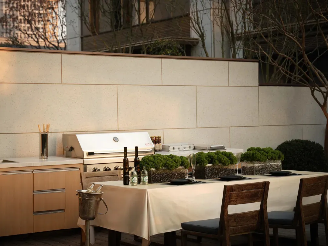 An outdoor kitchen with a concrete countertop and grill, featuring wooden chairs and greenery.