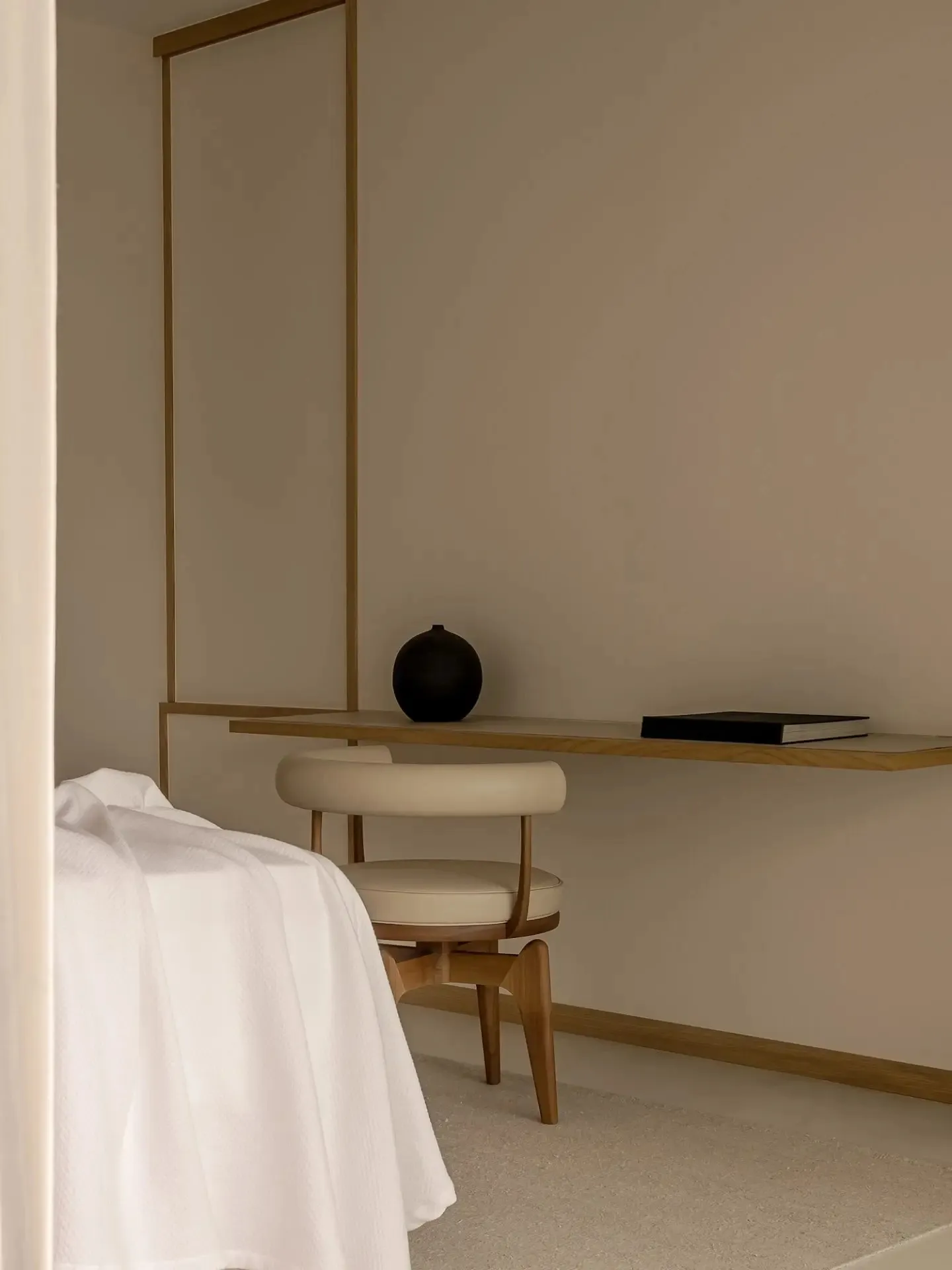 A minimalist bedroom with a white bed placed on textured wallpaper, featuring a floating desk with a modern chair.