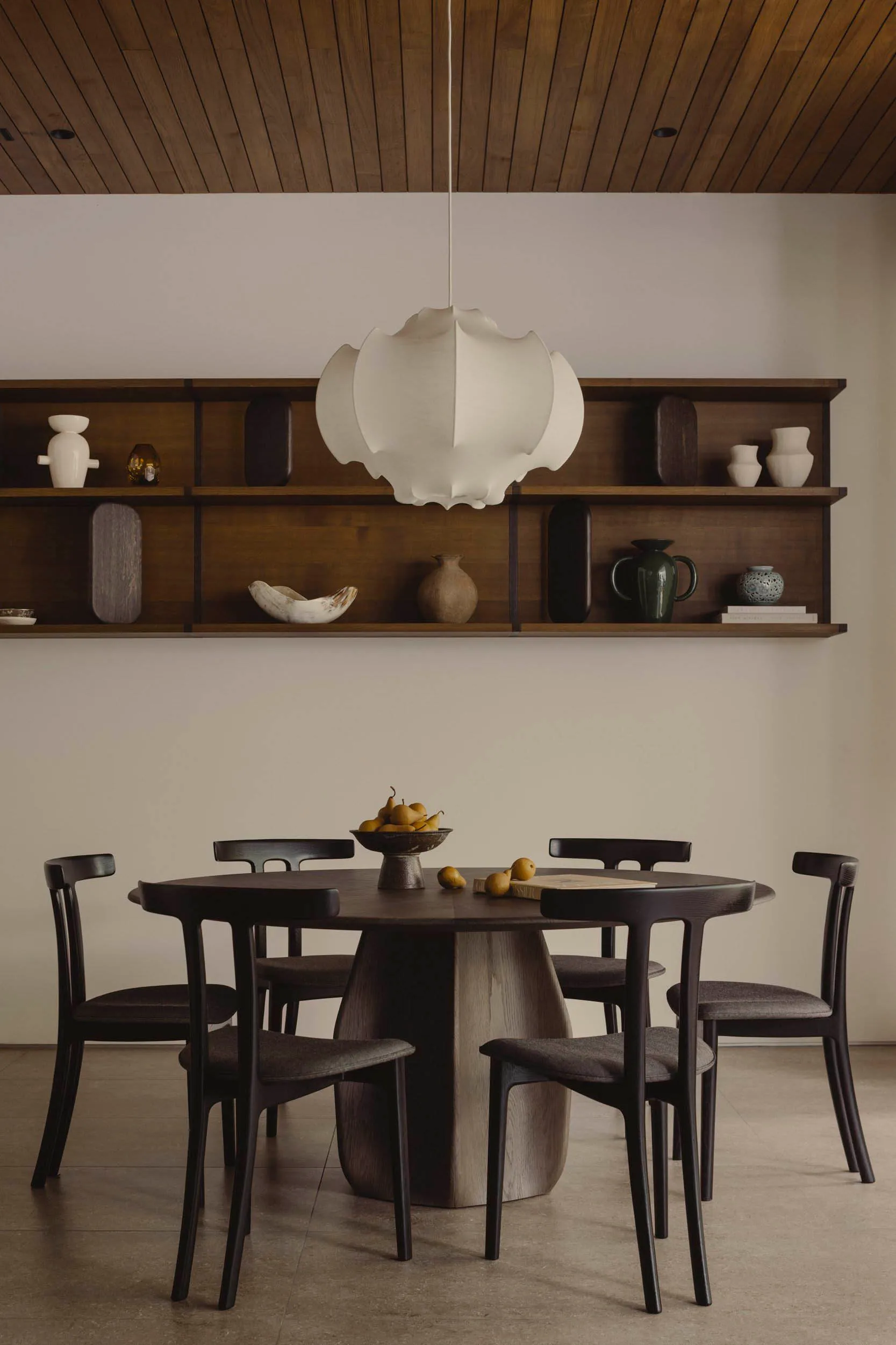 Modern dining room with wooden furniture, pendant light fixture, and wall-mounted shelves.