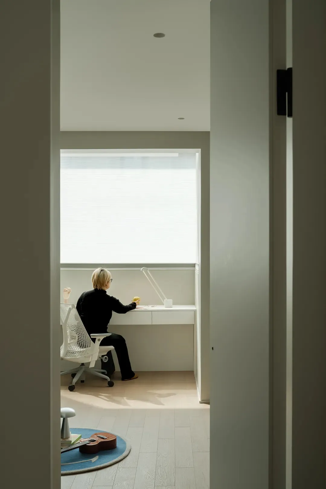 A modern home office desk setup with a person sitting at it, illuminated by a lamp.