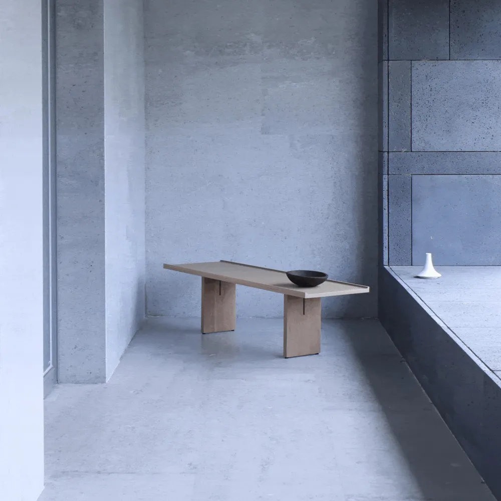 A minimalist concrete bench with a bowl on top, in a concrete-walled room with a white floor.