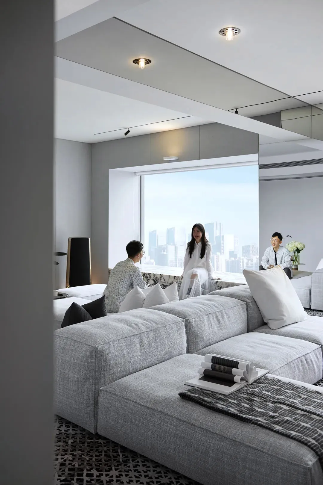 A modern living room featuring fabric couches, marble flooring, and a double-height window overlooking a cityscape.