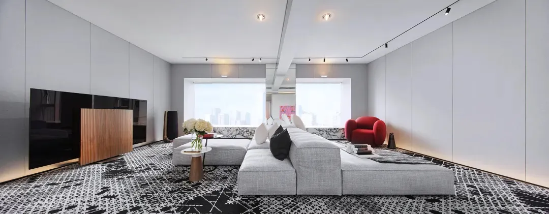 Modern living room with grey sofa, black and white patterned rug, large windows, and cityscape view.
