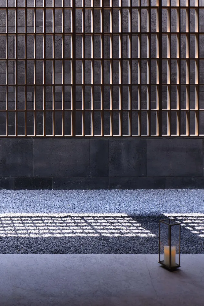 A close-up view of a metallic fence with concrete base casting shadows on the ground.