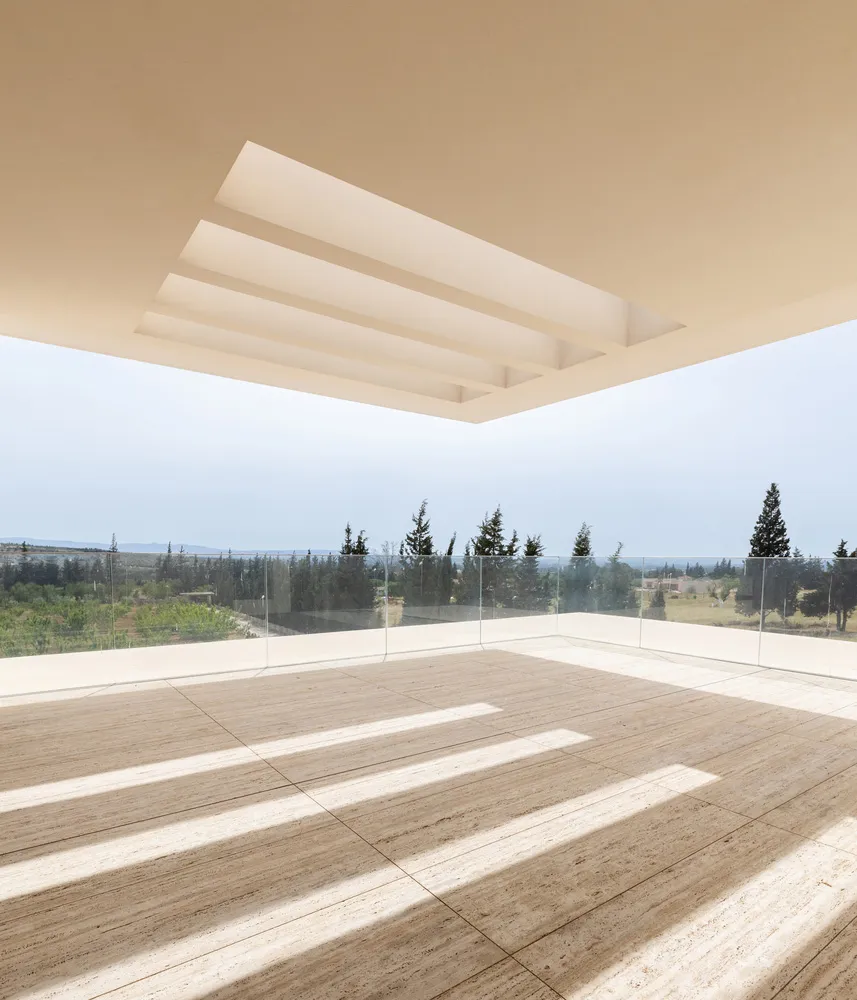 Modern minimalist indoor balcony with concrete floor and clear glass railing overlooking a scenic outdoor landscape.