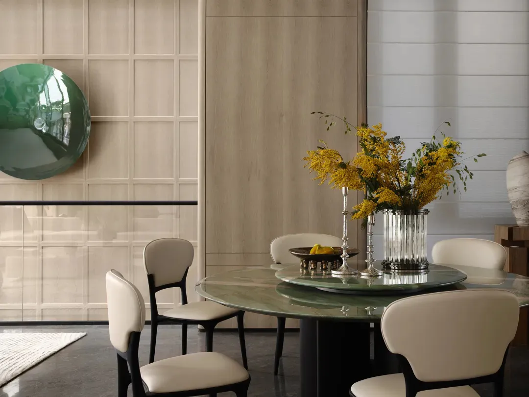 Modern dining room featuring a round glass-top table surrounded by white chairs, with a vase of yellow flowers and a green de