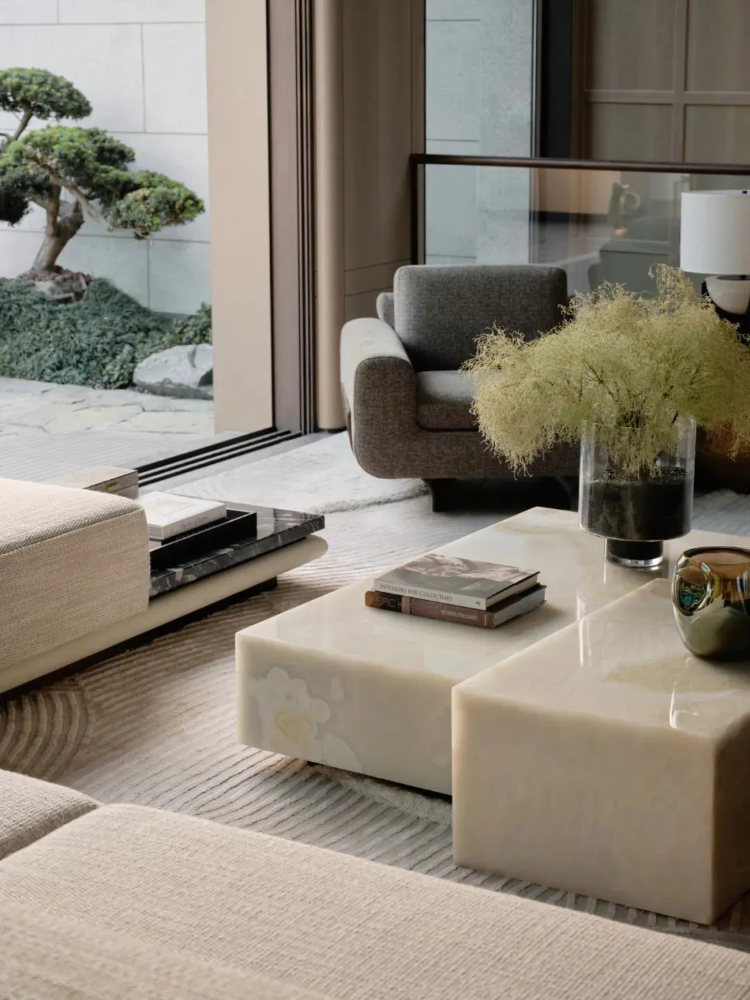 Modern living room with a marble table, beige sofa, and a bonsai tree outside the window.