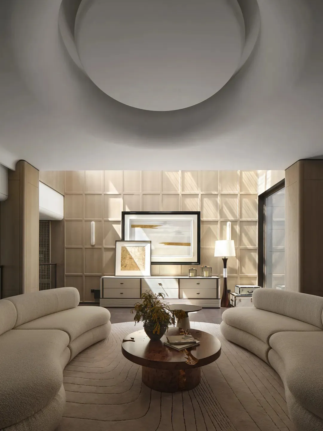 A modern interior living room with curved sofas, a round wooden coffee table, and a minimalist art gallery wall.